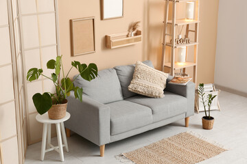Grey sofa with houseplants, wooden rack and lamps in living room