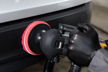 Man polishing car with orbital polisher indoors, closeup