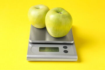 Electronic kitchen scale with apples on yellow background, closeup
