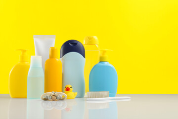 Baby cosmetic products and bath accessories on table against yellow background. Space for text