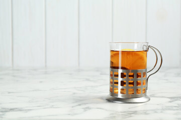 Glass cup of tea in metal holder on white marble table. Space for text