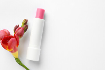 Lip balm and freesia flowers on white background, top view. Space for text
