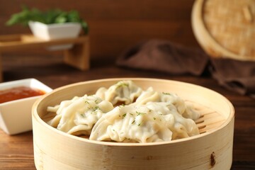Tasty boiled gyoza (dumplings) in bamboo steamer and sauce on wooden table, closeup