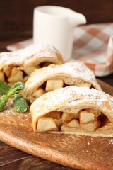 Pieces of tasty apple strudel with powdered sugar and mint on wooden table, closeup