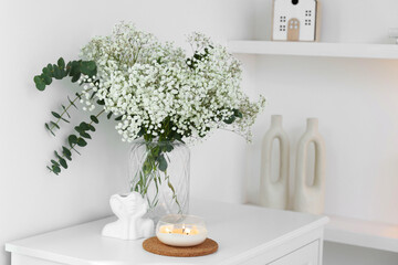 Bouquet of beautiful gypsophila flowers and eucalyptus branches in vase near decorative elements on...