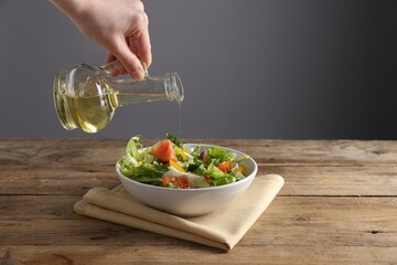 Woman pouring balsamic vinegar onto salad at wooden table against grey background, closeup. Space for text