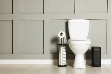 Ceramic toilet bowl, paper and trash can near grey wall indoors