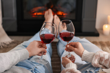 Couple with glasses of wine near fireplace on floor at home, selective focus