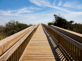 Long wood bridge leading to beach houses on the East Coast during a sunny day with beautiful blue...
