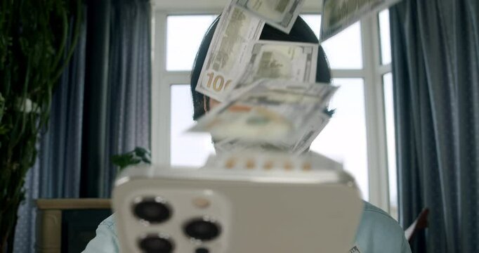 The man make money online. Money rain flow from the smartphone. Cash flow, dollar bills floating in the man face. Online winning. Business making easy money online concept. Happy, surprised earning