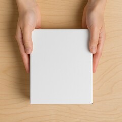 Obraz premium Hands Holding Blank White Book on Wooden Table – Top View