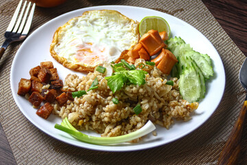 A plate of Thai-style fried rice with a fried egg, sliced cucumber, and sausage. The fried rice is garnished with green onions and crispy croutons. 