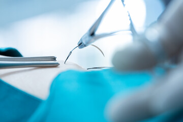 Doctor hand wear sterile gloves and surgery scissor stitching up wound after surgery.Plastic surgeon placing sutures after plastic surgery in operating room.Nurse teaches the technique of suturing.