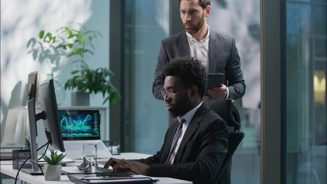 African American man employee working computer Caucasian boss leader manager come checking work support businessmen business office men males pc diversity guys mentor tap on shoulder workers coworkers