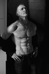 Fototapeta premium Slim muscular male model on black background. Shirtless fitness guy in black sweatpants posing in studio. Man with six pack abs in sunset light. Brutal photo
