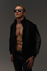 Slim muscular male model on black background. Shirtless fitness guy in black sweatpants posing in studio. Man with six pack abs in sunset light. Brutal photo