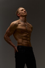 Fototapeta premium Slim muscular male model on black background. Shirtless fitness guy in black sweatpants posing in studio. Man with six pack abs in sunset light. Brutal photo