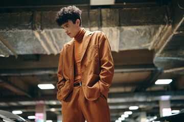 Stylish young man in a brown suit poses confidently in a modern underground parking garage Warm tones enhance the fashion forward look
