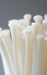 A close-up photograph of white enoki mushrooms against a light gray background, with blank space at the top and bottom for text. The composition is symmetrical, focusing on one side of the image. 