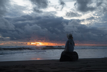 A woman sits alone and enjoys the view of the beach at sunset