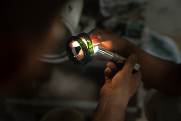 A craftsman shines a light on a piece of jade to see its clarity. A skilled craftsman cuts jade to...