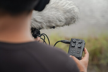 A man records audio outdoors with a handy recorder connected to a shotgun microphone