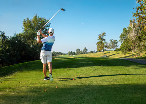 A wide shot of a man swinging a golf club looking down the fairway at a golf course