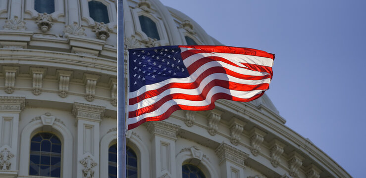 The flag of the United States waves over the Capitol dome. The state capitol buildings with flag. The Capitol near US flag. The Congress. American flag waving. The Capitol Hill in Washington, DC.