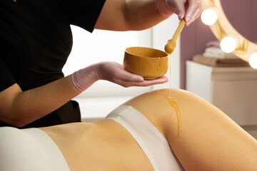 Honey flows smoothly from dipper during wellness skin treatment. Honey detox massage or caramel liposuction