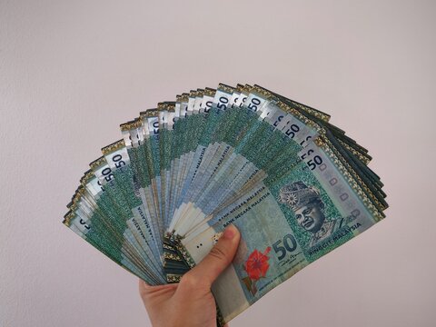 A hand holding RM50 Malaysian Ringgit banknotes against a white background. Suitable for business, financial, savings, investment, and economic use. 