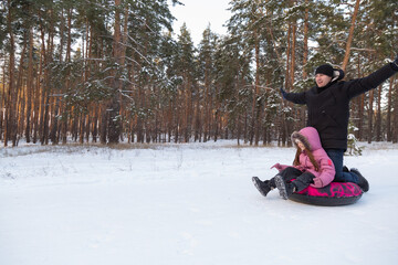 Father and daughter having fun with snow tube in the forest