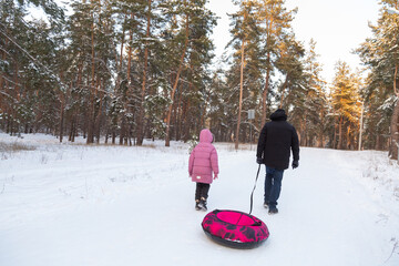 Father and daughter having fun with snow tube in the forest