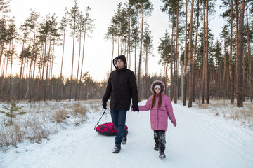 Dad with his daughter walking with snow tubing in the winter forest