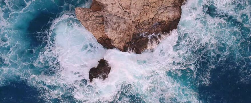 Top-down, drone shot of the sea waves crashing on a rock on the shore of Fethiye, Turkey at sunset