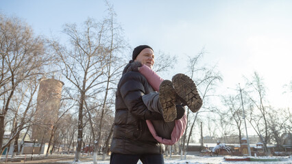Grandfather playing with her granddaughter on the playground in the park in winter