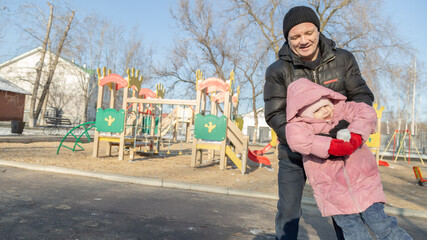 Grandfather playing with her granddaughter on the playground in the park in winter