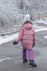 Happy child walks down the street and enjoys the first snow in winter