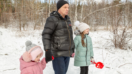Little girls with her grandfather walk in a snowy forest, have fun together