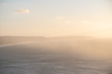Fototapeta premium Atlantic ocean coast in Nazare, Portugal. Pink clouds over the ocean at foggy sunset.