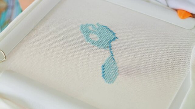 Close-up of a hand skillfully cross-stitching a light blue pattern on fabric. Needle embroidery stitches demonstrating the art of needlework