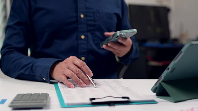 Analyzing Financial Data Person In Blue Shirt Reviews Document With Pen, Calculator, Clipboard, Tablet Screen Boosting Productivity Reviewing Statistics On Medium