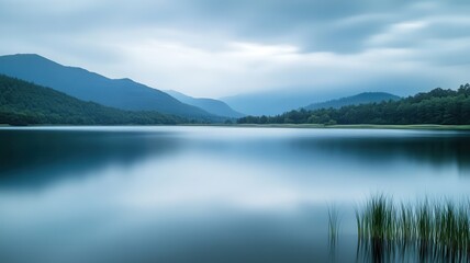 Fototapeta premium Calm lake, misty mountains, serene dawn