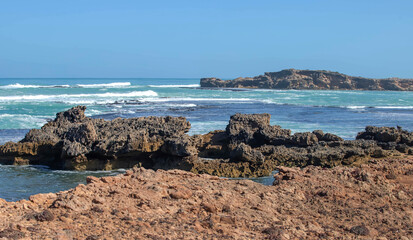 Sharp coastal rock formations and turquoise ocean waves meet on the rugged shoreline of South...