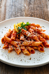 Penne noodles with tomato sauce and parmesan cheese served on wooden table	