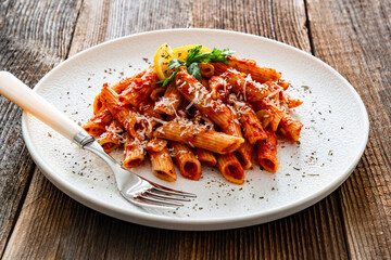 Penne noodles with tomato sauce and parmesan cheese served on wooden table	