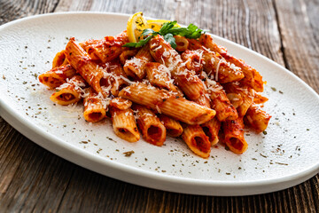 Penne noodles with tomato sauce and parmesan cheese served on wooden table	