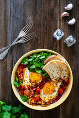 Shakshuka - fried eggs with vegetables on wooden table	