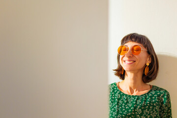 Woman face. Portrait of gorgeous girl with beautiful earrings and orange sunglasses, smiling at camera, looking confident and cheerful.