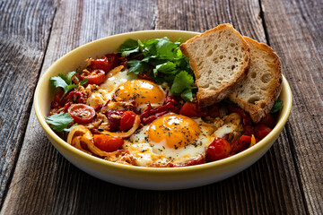 Shakshuka - fried eggs with vegetables on wooden table	