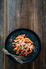 Penne noodles with tomato sauce, black olives and parmesan cheese served on wooden table	